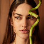 Female model with clear skin behind a green plant
