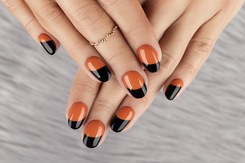 Manicured woman's hand over furry background. Trendy autumn halloween orange nail design.