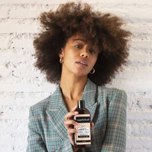 Eine wunderschöne Frau mit lockigem Haar hält das Nr.1 Shampoo von Nuggela & Sulé in der Hand