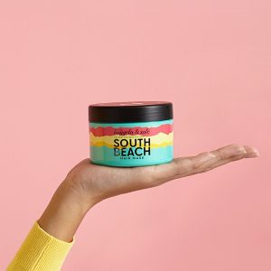 Eine Hand hält die South Beach Maske von Nuggela & Sulé vor einem pinken Hintergrund