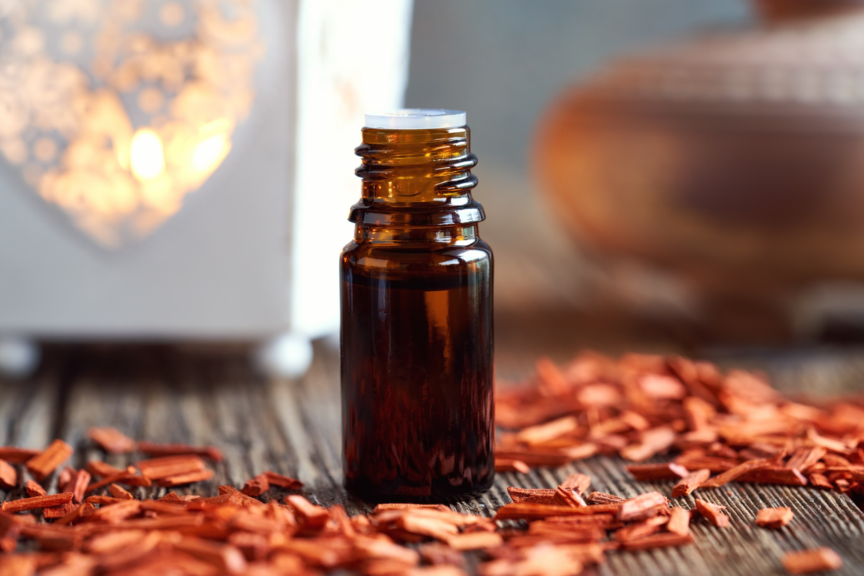 A bottle of aromatherapy essential oil with pieces of red sandalwood A dark bottle of aromatherapy essential oil with red sandalwood chips and a candle in the background