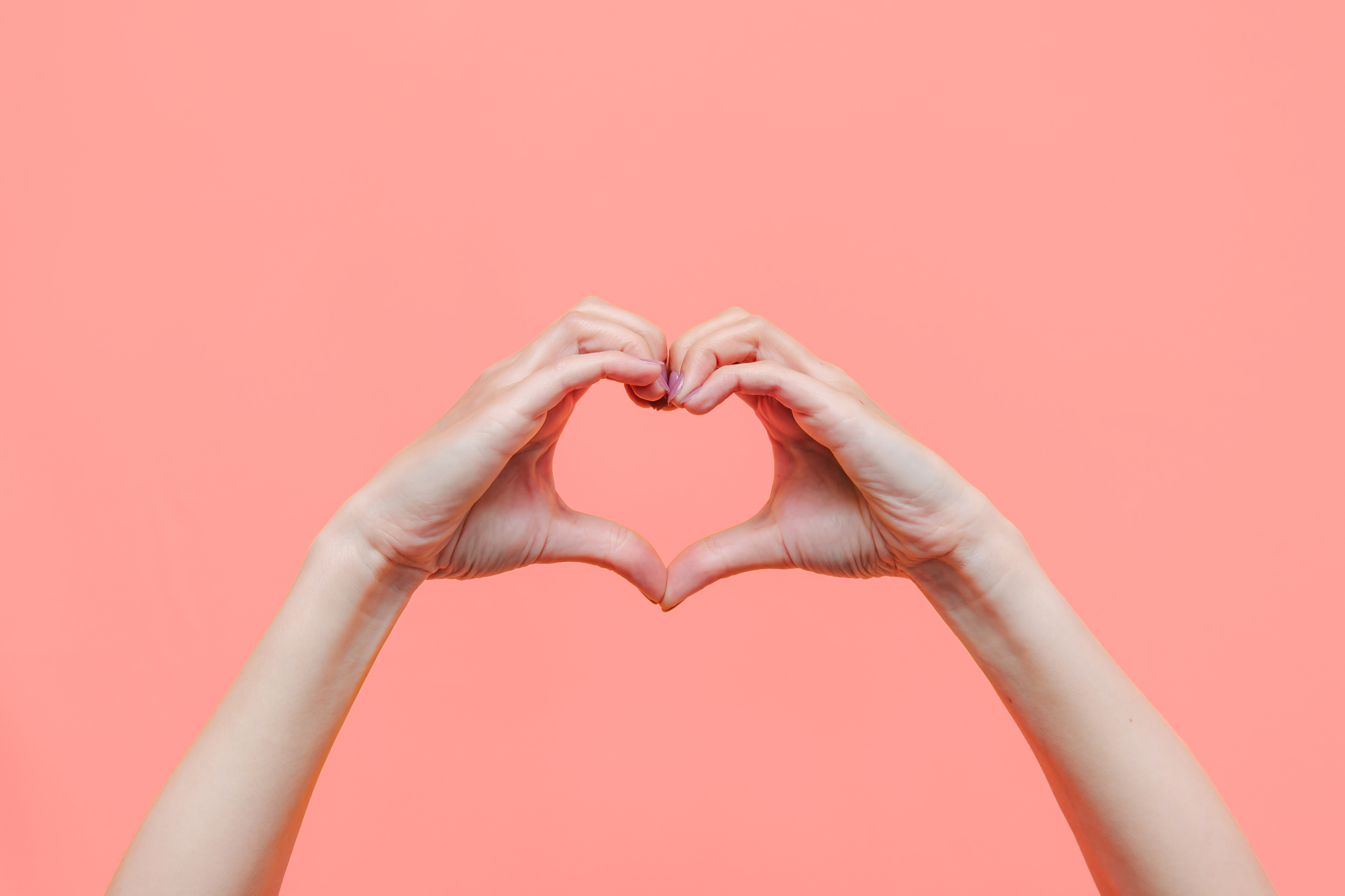 Female hands showing a heart shape isolated on a color light pink background Female hands showing a heart shape isolated on a color light pink background. Sign of love, harmony, gratitude, charity. Feelings and emotions concept