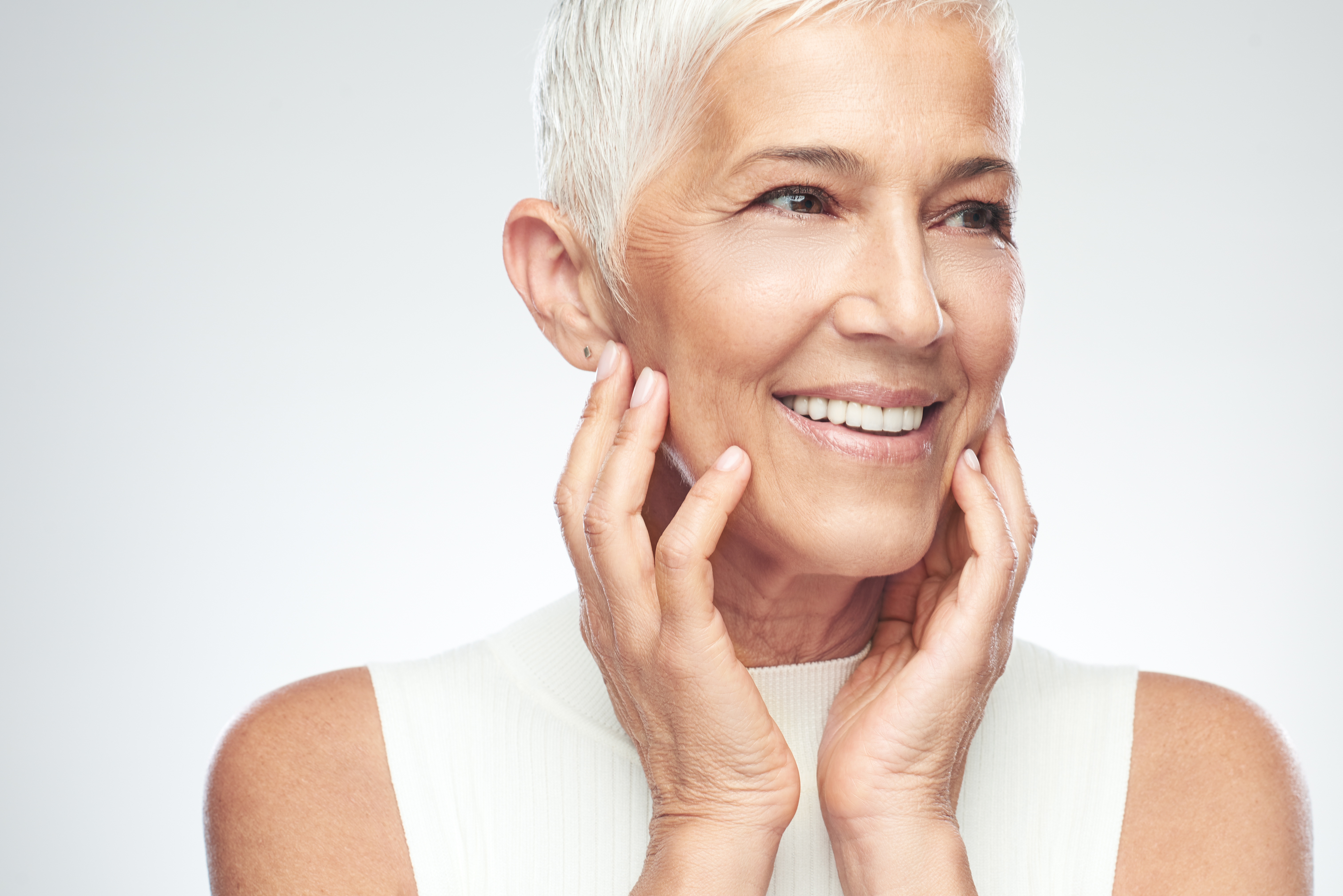 Woman posing in front of gray background. Beautiful smiling senior woman with short gray hair posing in front of gray background. Beauty photography.