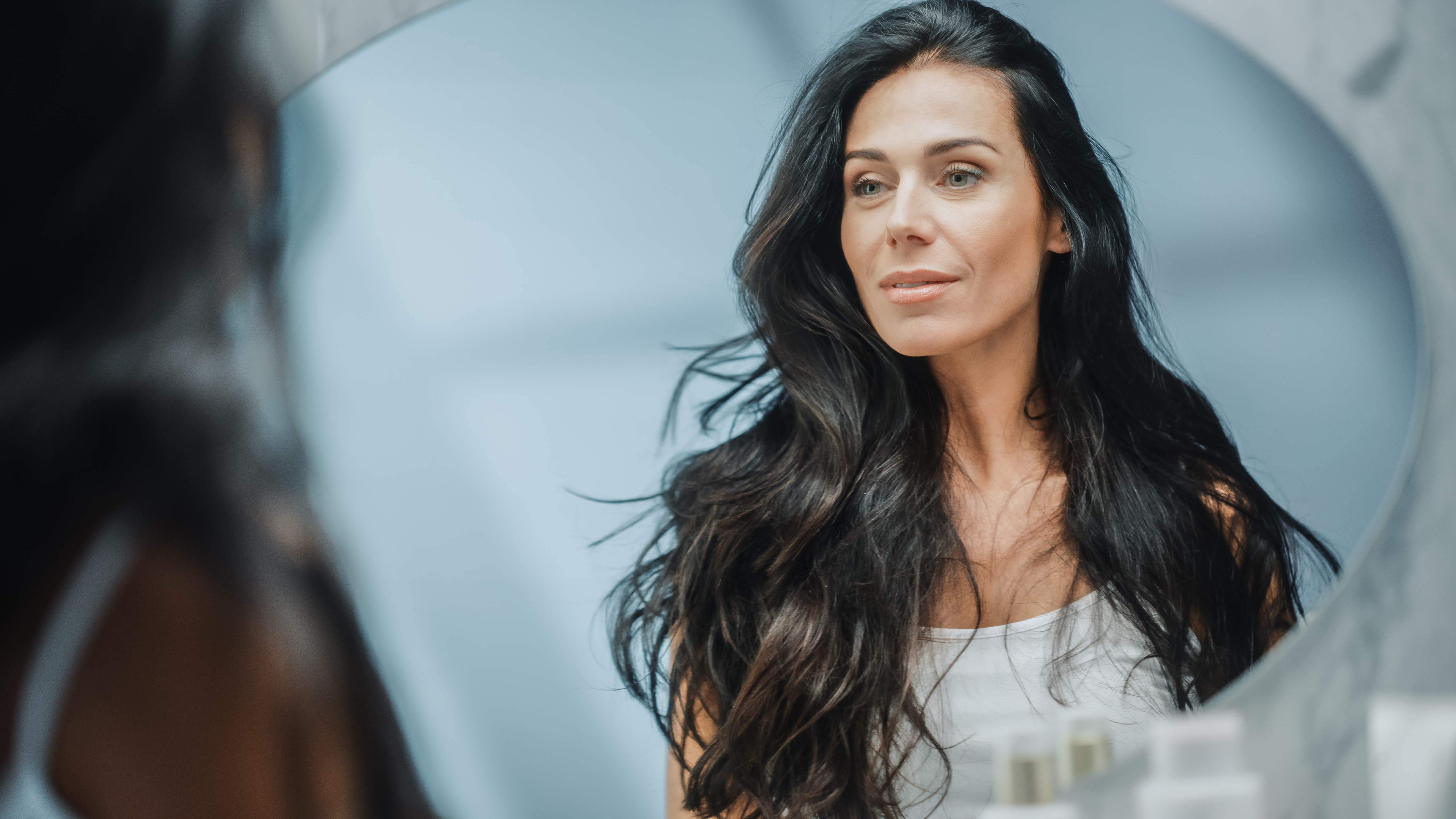 Beautiful Caucasian Middle Aged Woman Looks into Bathroom Mirror, Enjoys Her Looks. Concept for Happiness, Wellbeing, Natural Beauty and Organic Skin Care Products Beautiful Caucasian Middle Aged Woman Looks into Bathroom Mirror, Enjoys Her Looks. Concept for Happiness, Wellbeing, Natural Beauty and Organic Skin Care Products