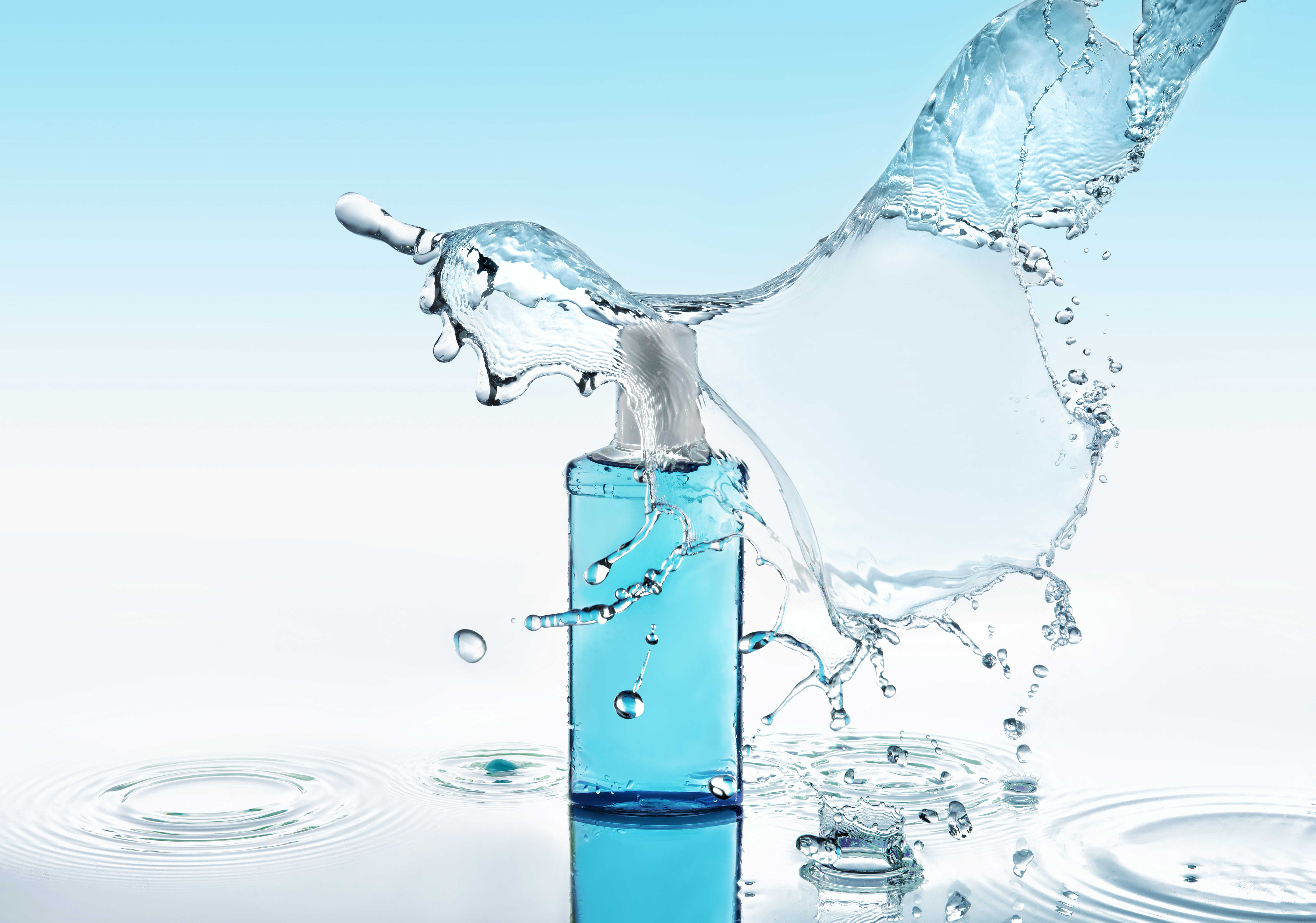 Moisturizing shampoo on the blue water background with big splash Blue moisturizing shampoo stays on the blue water background with big splash above the bottle and with many water drops and water waves around the bottle