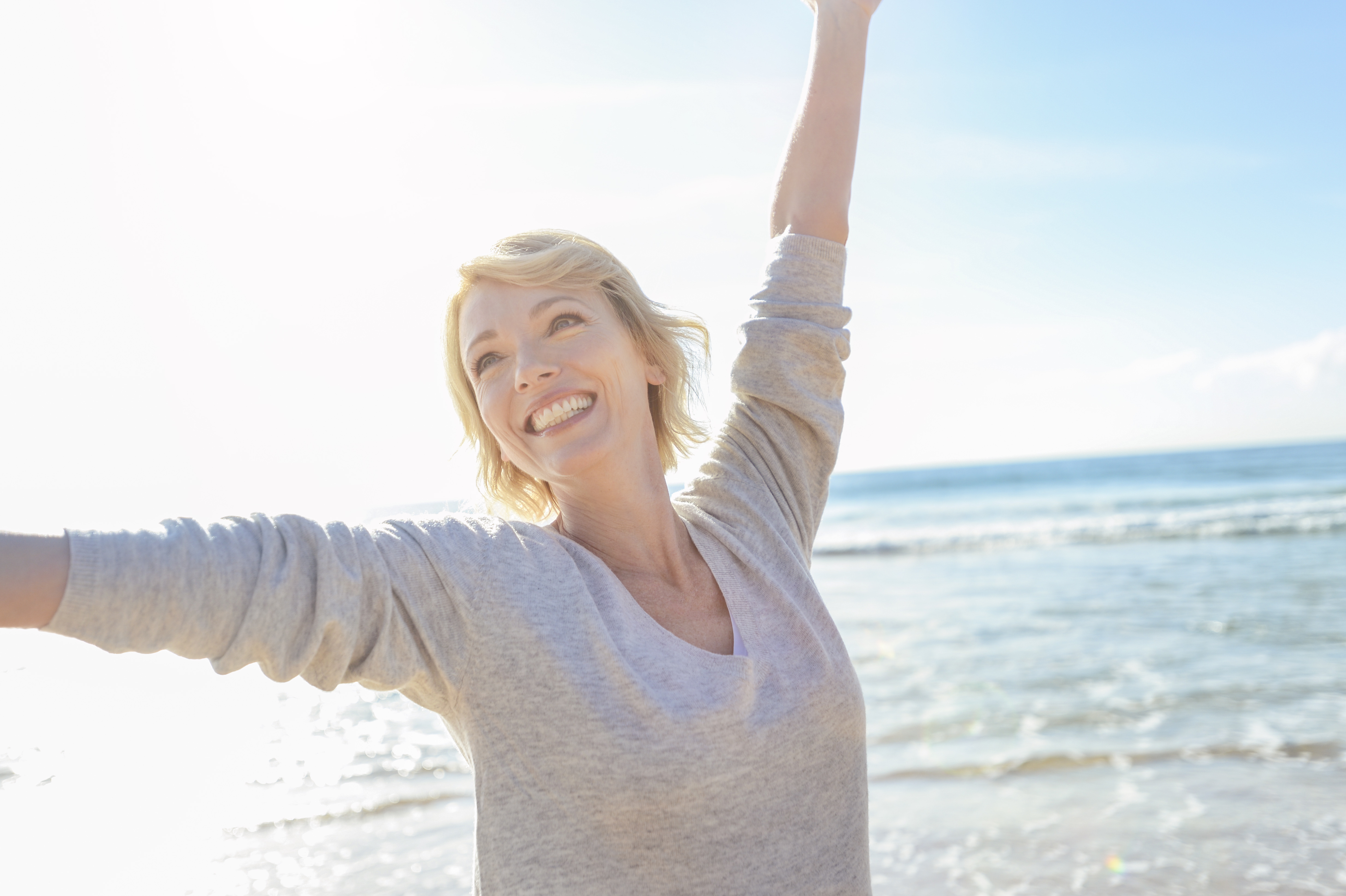 Mature woman on the beach with arms up. Mature woman on the beach with arms up. She looks very happy and relaxed. She is smiling and joyful with the ocean behind her. Bright sunny summer day