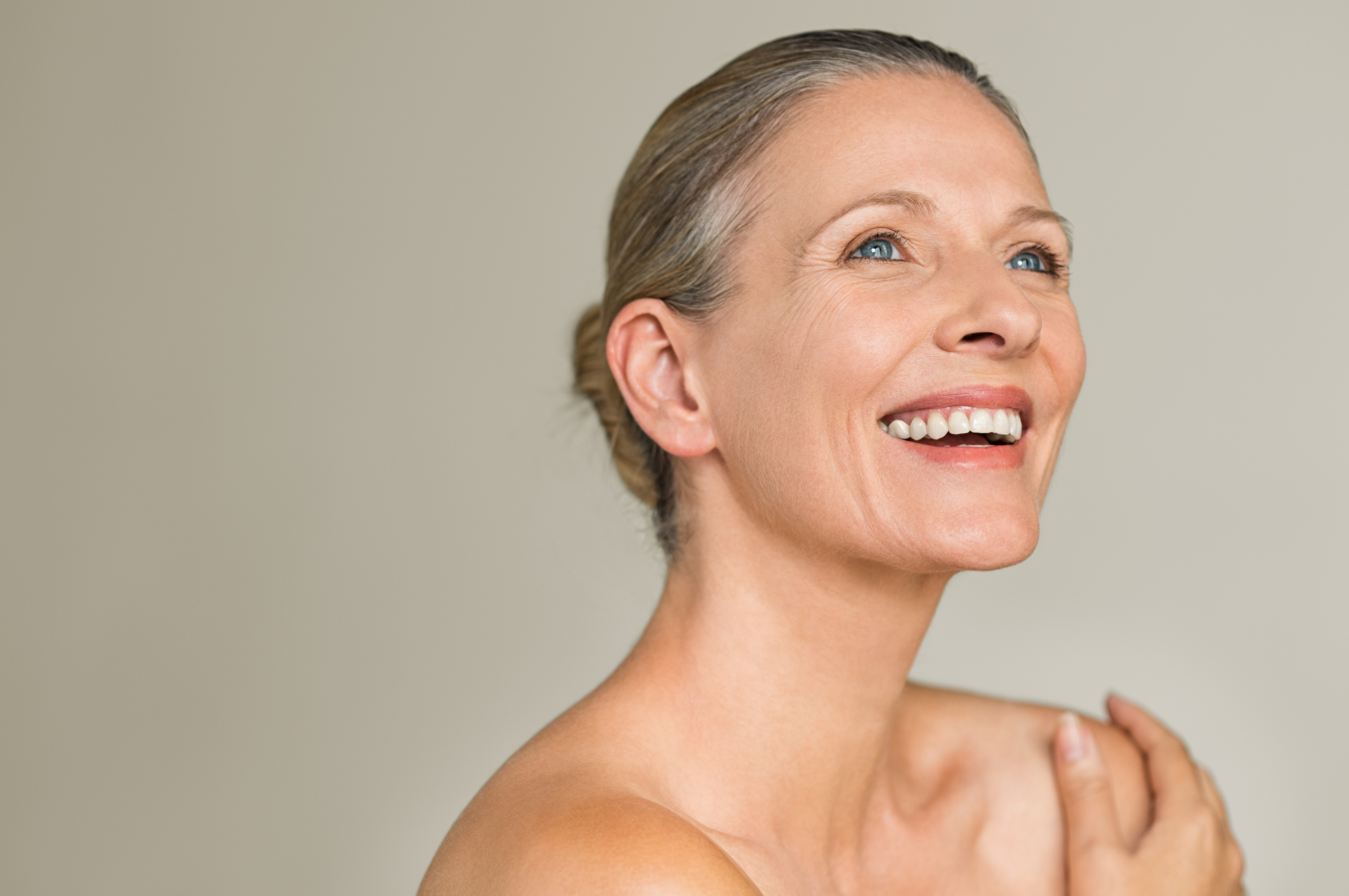 Beauty mature woman laughing Portrait of a cheerful senior woman smiling while looking away isolated on gray background. Happy mature woman after spa massage and anti-aging treatment on face.