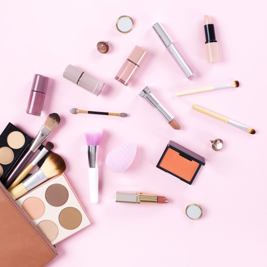 Makeup bag with cosmetic products spilling out on to a soft pink background