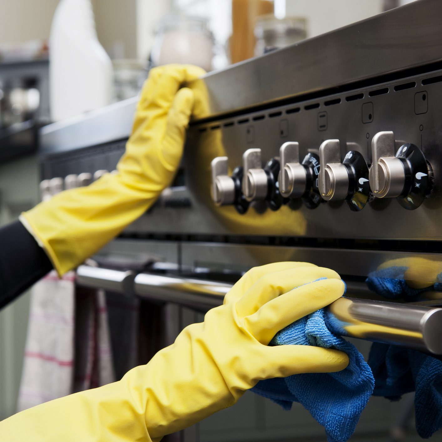 Closeup photograph of two hands cleaning the oven in a domestic kitchen.